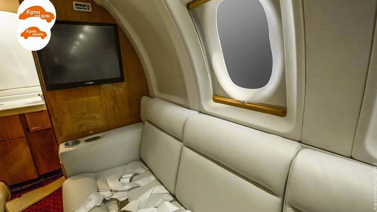 Samolyoty Hawker 800 — Интерьер самолета: светлые сиденья с ремнями безопасности и телевизор на деревянной панели