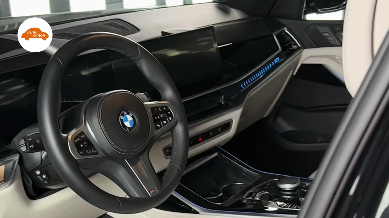 Интерьер BMW с бежевыми кожаными сиденьями, черным рулем и синей амбиентной подсветкой