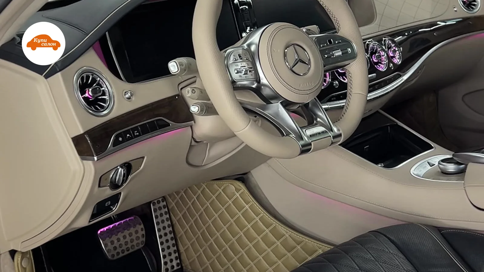 Интерьер Mercedes-Benz с бежевым рулем, черными сиденьями и бежевыми ковриками с ромбовидной прострочкой.
