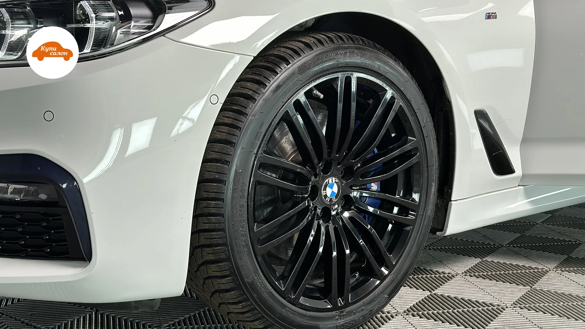 Белый BMW, вид спереди сбоку, черные диски, синие суппорта, на плитке