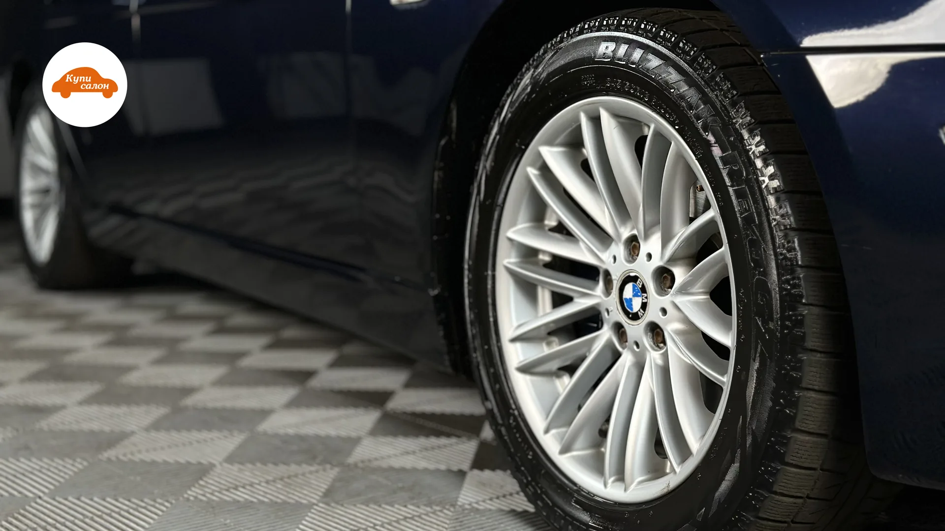 Деталь: колесо BMW с шиной Blizzak, вид сбоку, на фоне плиточного пола.