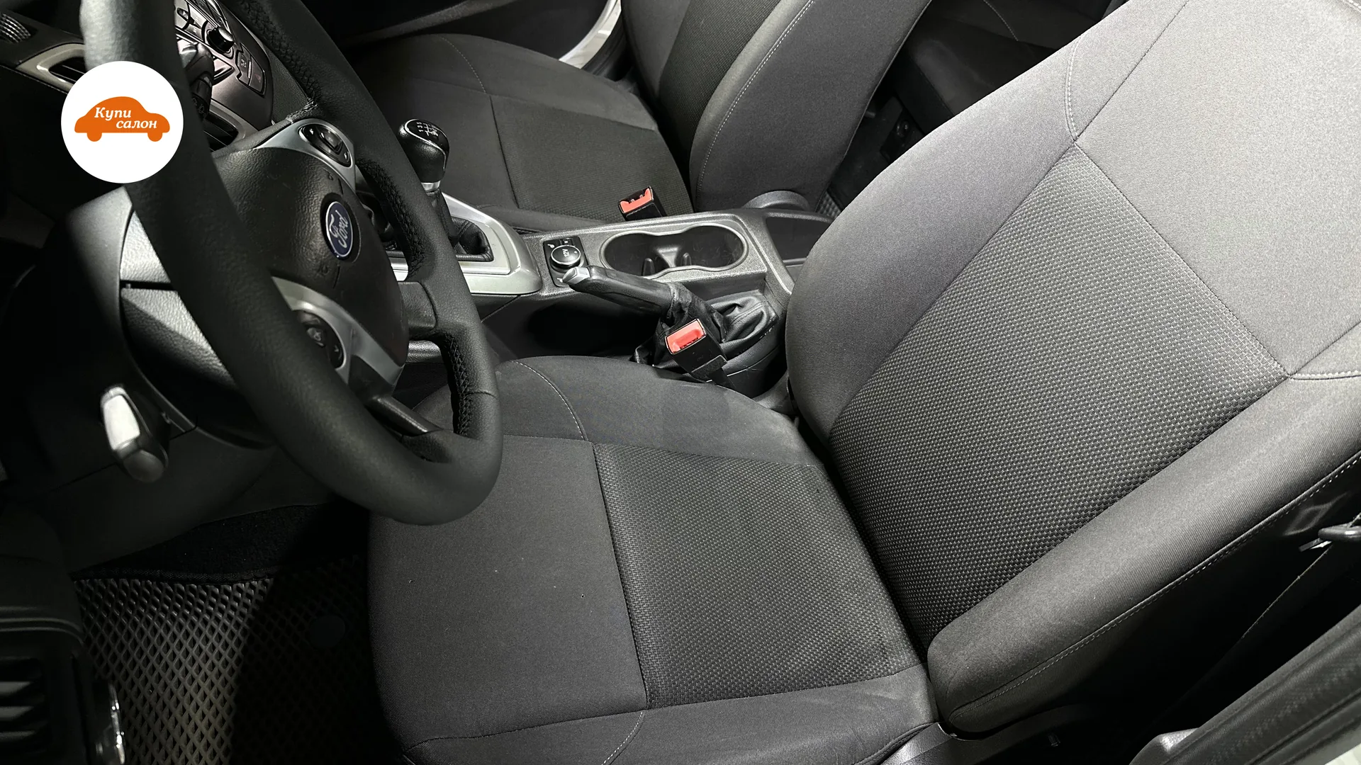 Интерьер Ford Focus с тканевыми сиденьями серого цвета, рулем с логотипом Ford и ручкой КПП.