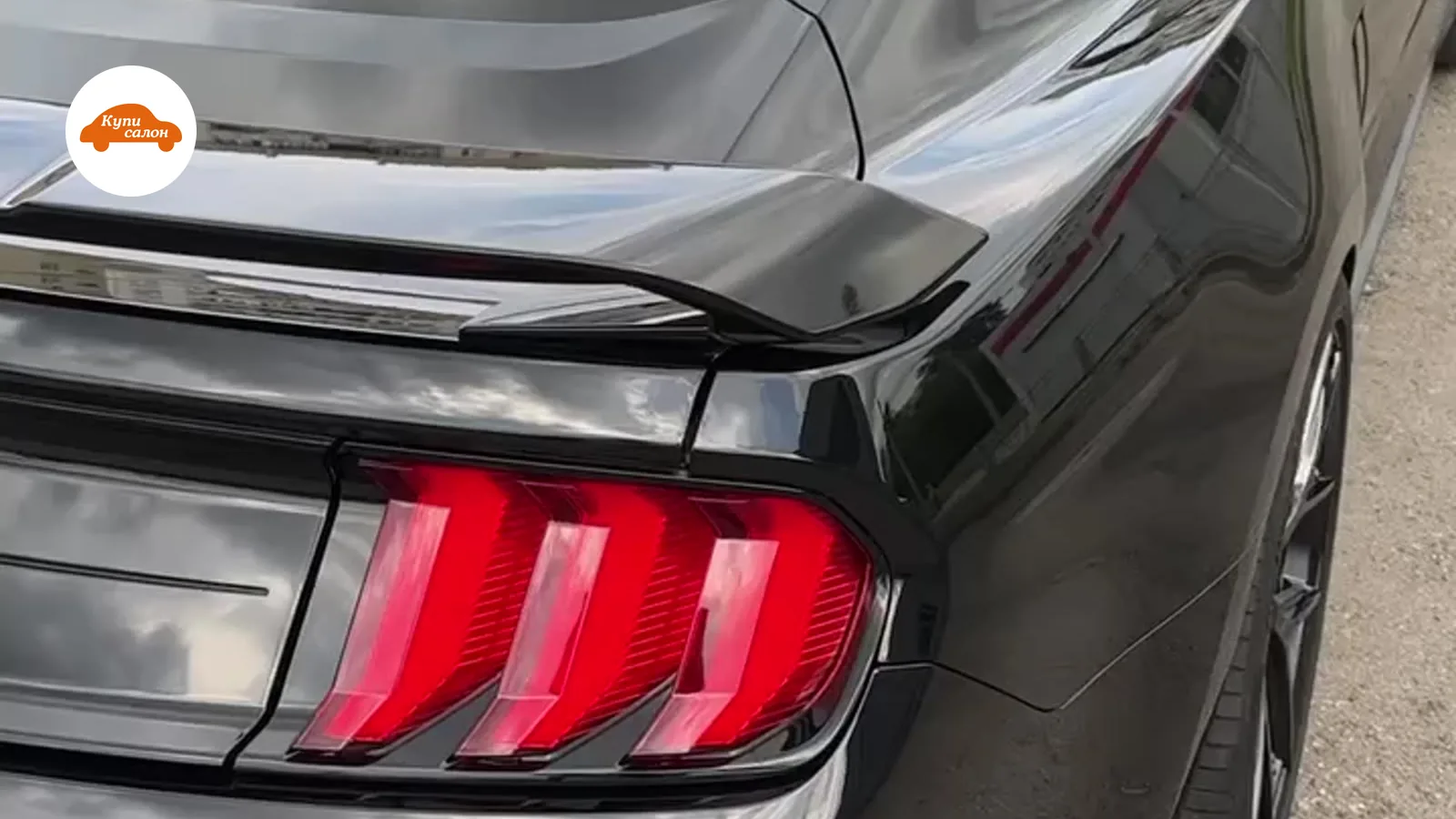 Задняя часть черного Ford Mustang, полировка кузова, спойлер, красные фонари.