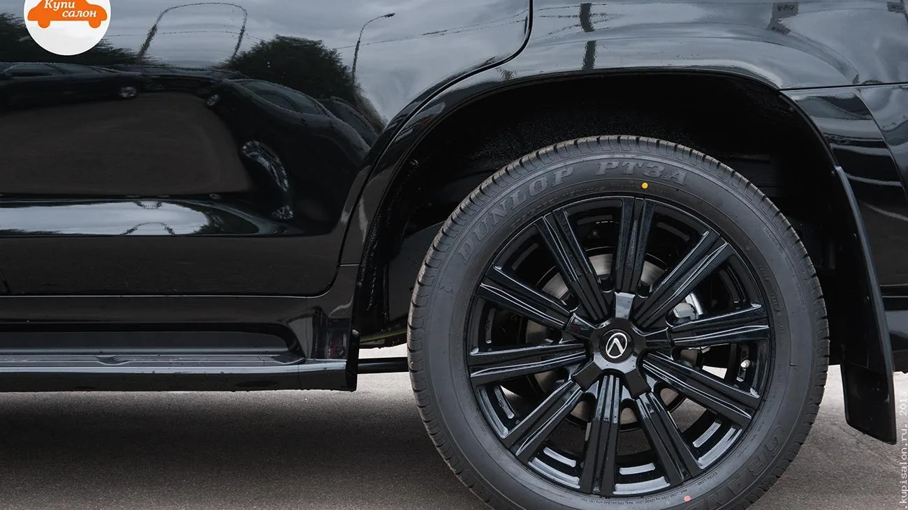 Деталь экстерьера черного автомобиля с черными дисками и шинами Dunlop.