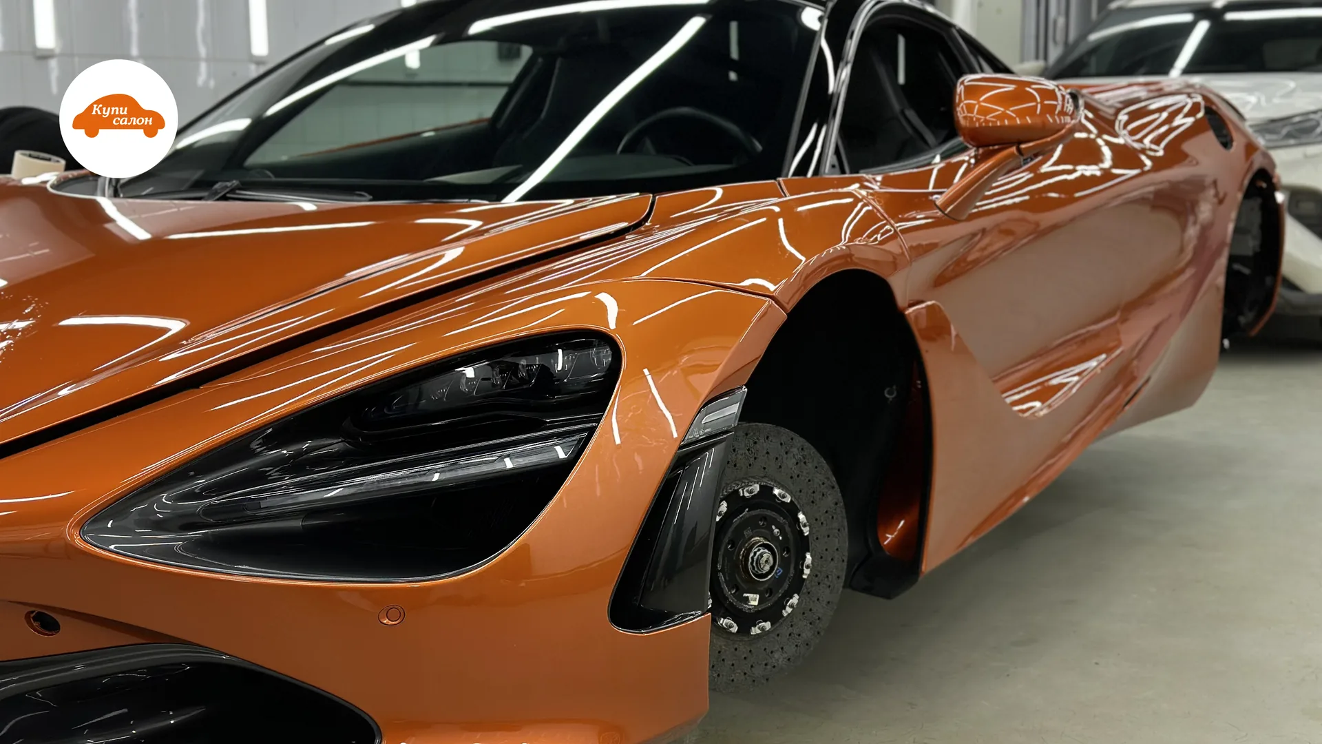Оранжевый спорткар McLaren 720S в процессе оклейки полиуретановой пленкой, без колеса, в автоателье.