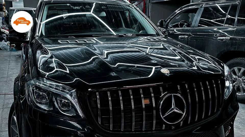 Черный Mercedes-Benz с хромированной решеткой радиатора, отражающей LED-освещение, в детейлинг-студии