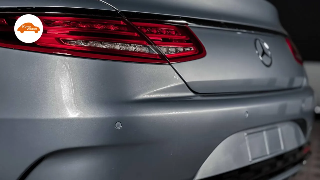 Задняя часть автомобиля Mercedes-Benz, видны задние фонари и бампер, кузов серого цвета с глянцевым блеском.