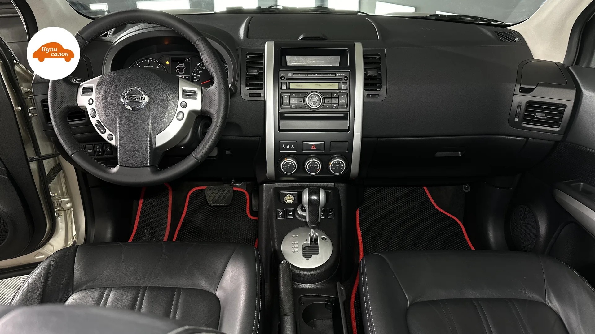 Интерьер Nissan с перетянутым рулем из черной перфорированной кожи, сиденьями из черной кожи с белой строчкой и черными ковриками с красной окантовкой