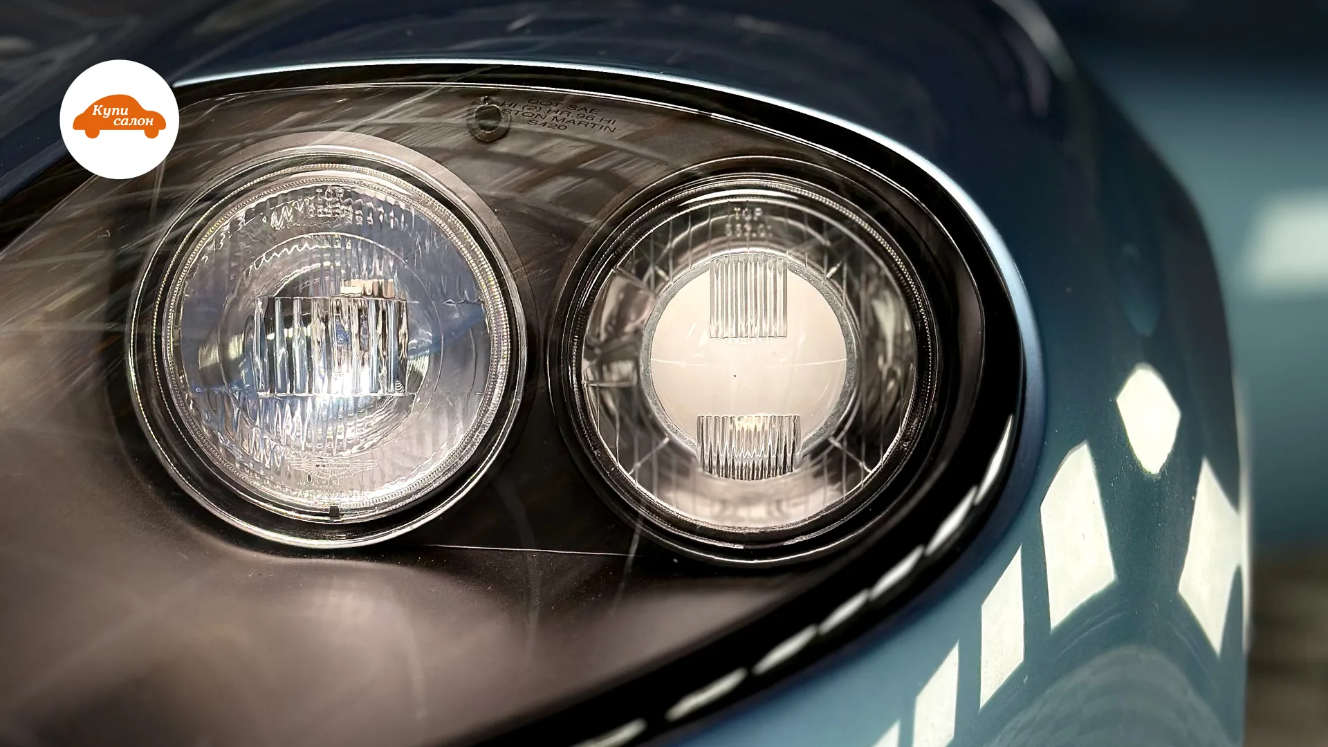 Крупный план фары автомобиля Aston Martin, синий цвет кузова, отражения света.