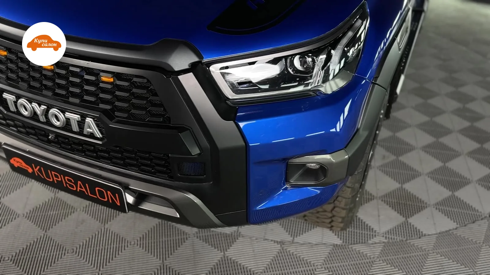 Передняя часть синего автомобиля Toyota с черной решеткой радиатора, фарами и логотипом Toyota