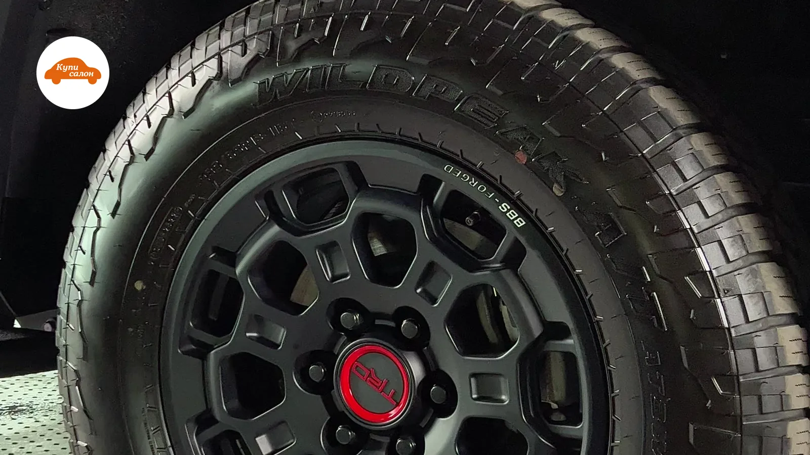 Колесо автомобиля с черным диском TRD Pro и шиной Wildpeak, камуфляжная оклейка кузова.