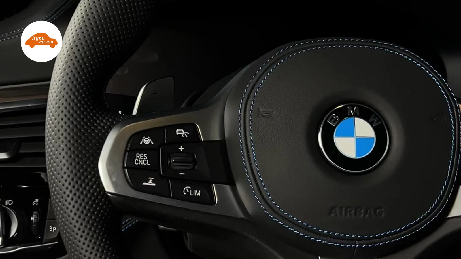 Интерьер BMW, руль перетянут черной перфорированной кожей с синей строчкой, видна кнопка подогрева руля