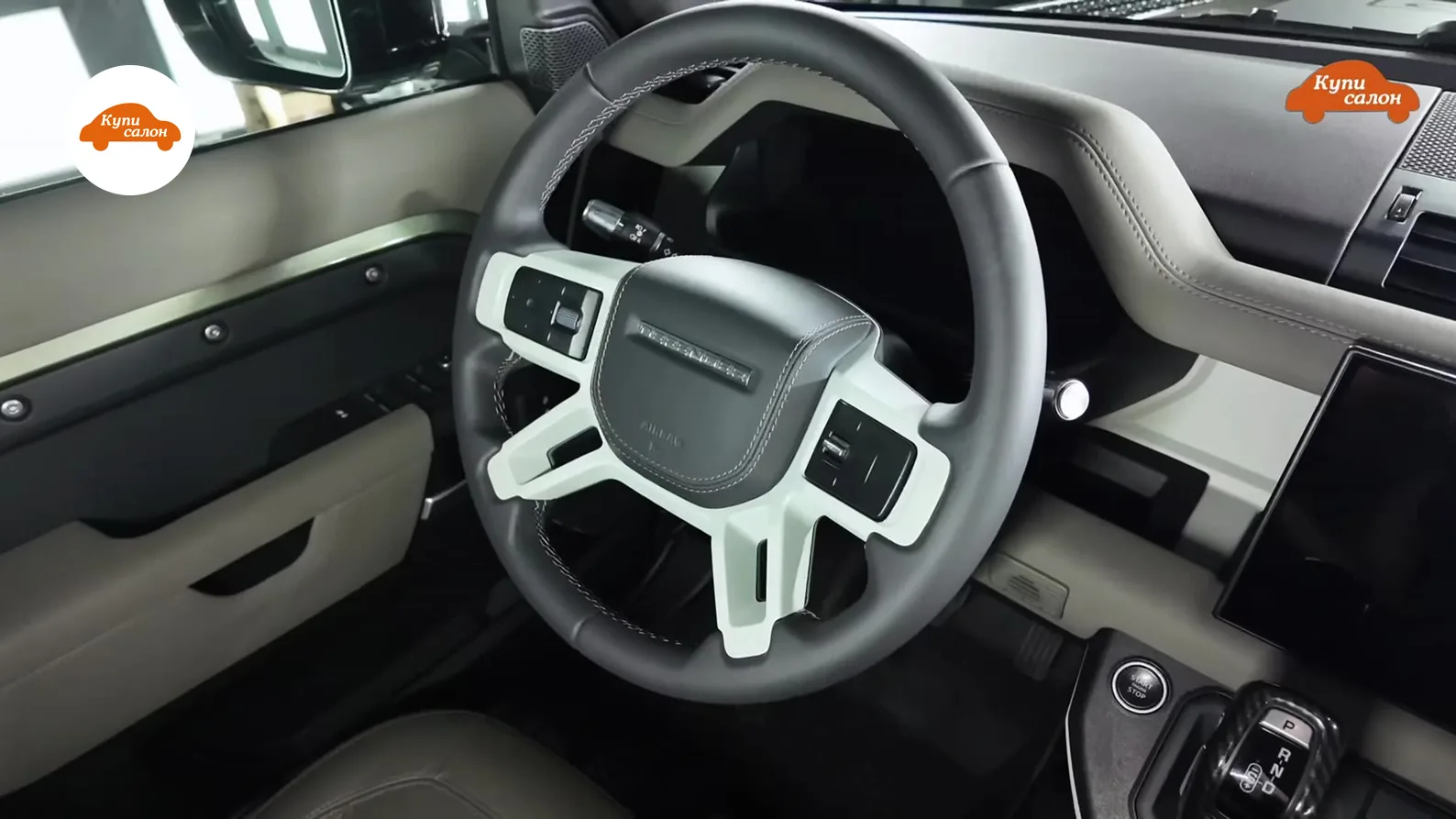 Интерьер Land Rover Defender с перетянутым рулем в серой коже и белыми вставками, бежевая обивка дверной карты и торпеды