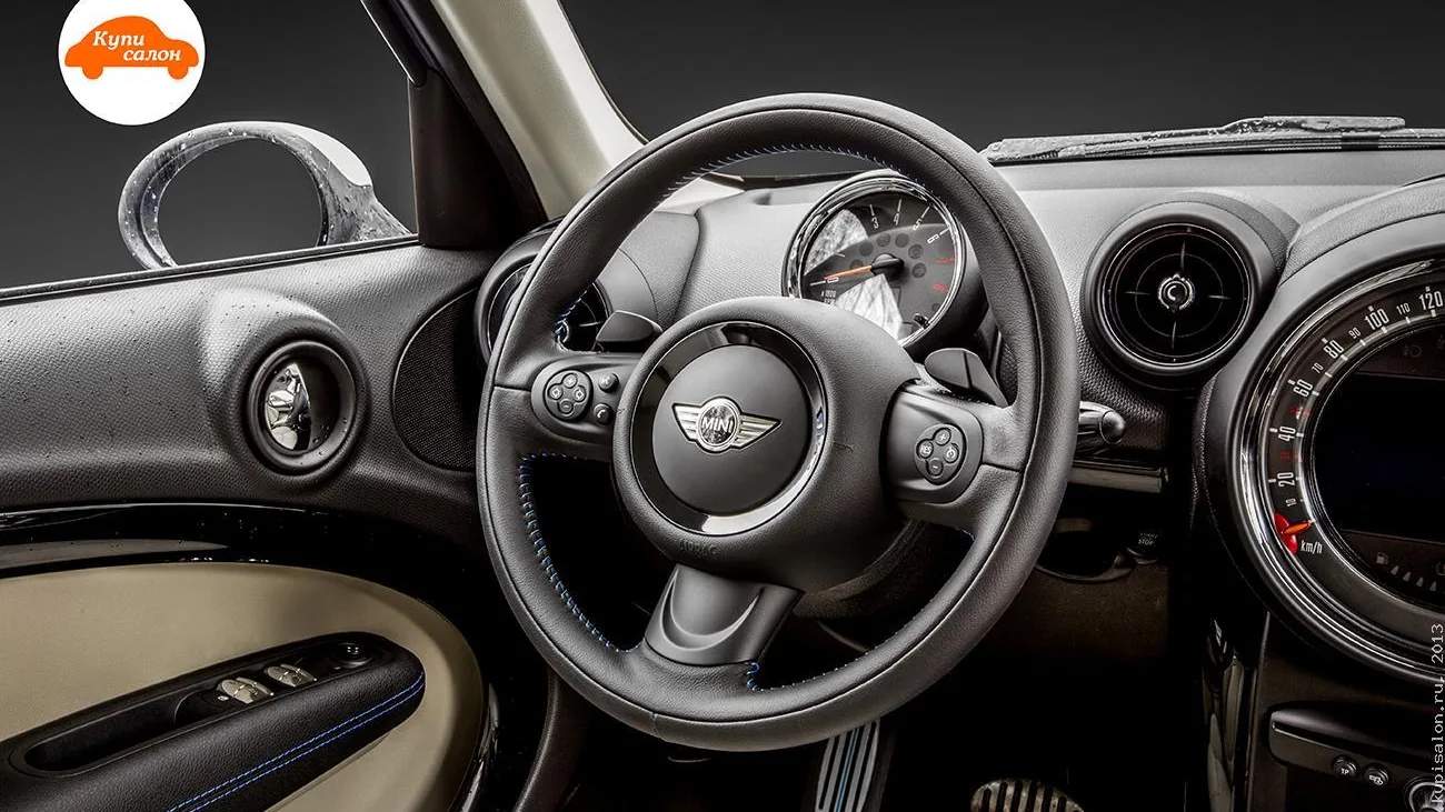 Интерьер Mini с перетянутым рулем черной кожей с синей строчкой и бежевыми вставками на дверях.