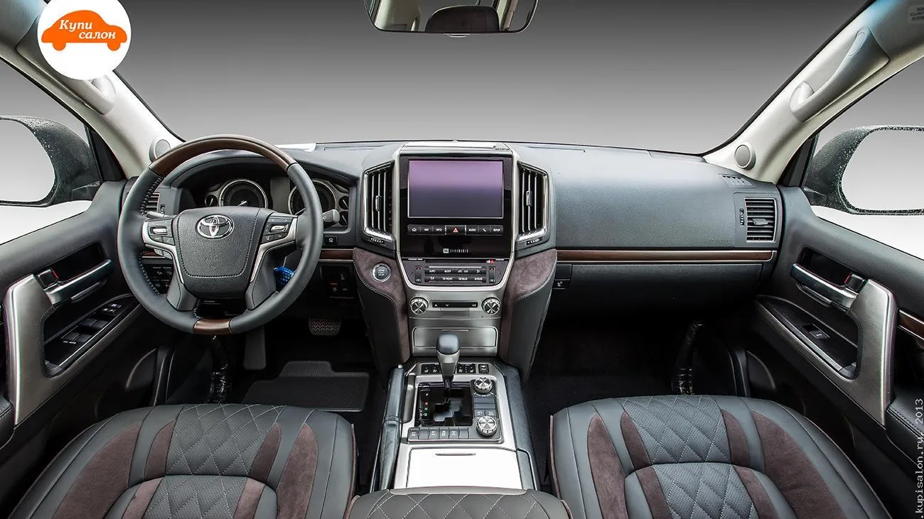 Салон Toyota Land Cruiser 200 после 2015 года: руль с эмблемой Toyota и вставками под дерево, панель и передние кресла с ромбовидной стёжкой