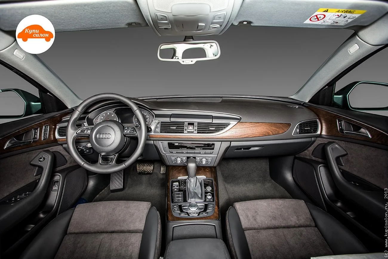 Салон Audi A6, вид с заднего ряда на переднюю панель: руль, центральная консоль с селектором, передние кресла с тёмной ворсовой серединой