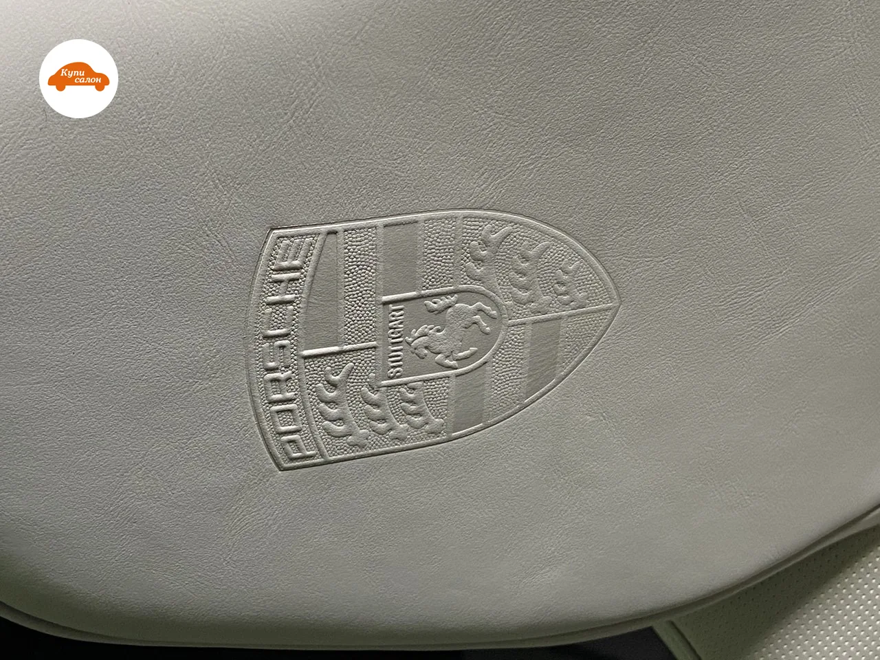 Рельеф оттиска герба Porsche на светло-серой коже вблизи: надпись PORSCHE, конь и полосы герба