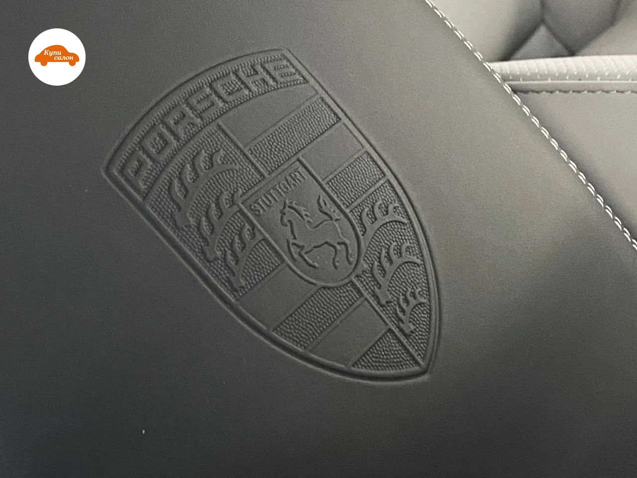 Герб Porsche выдавлен на чёрной коже с белой строчкой — тиснение на крышке подлокотника