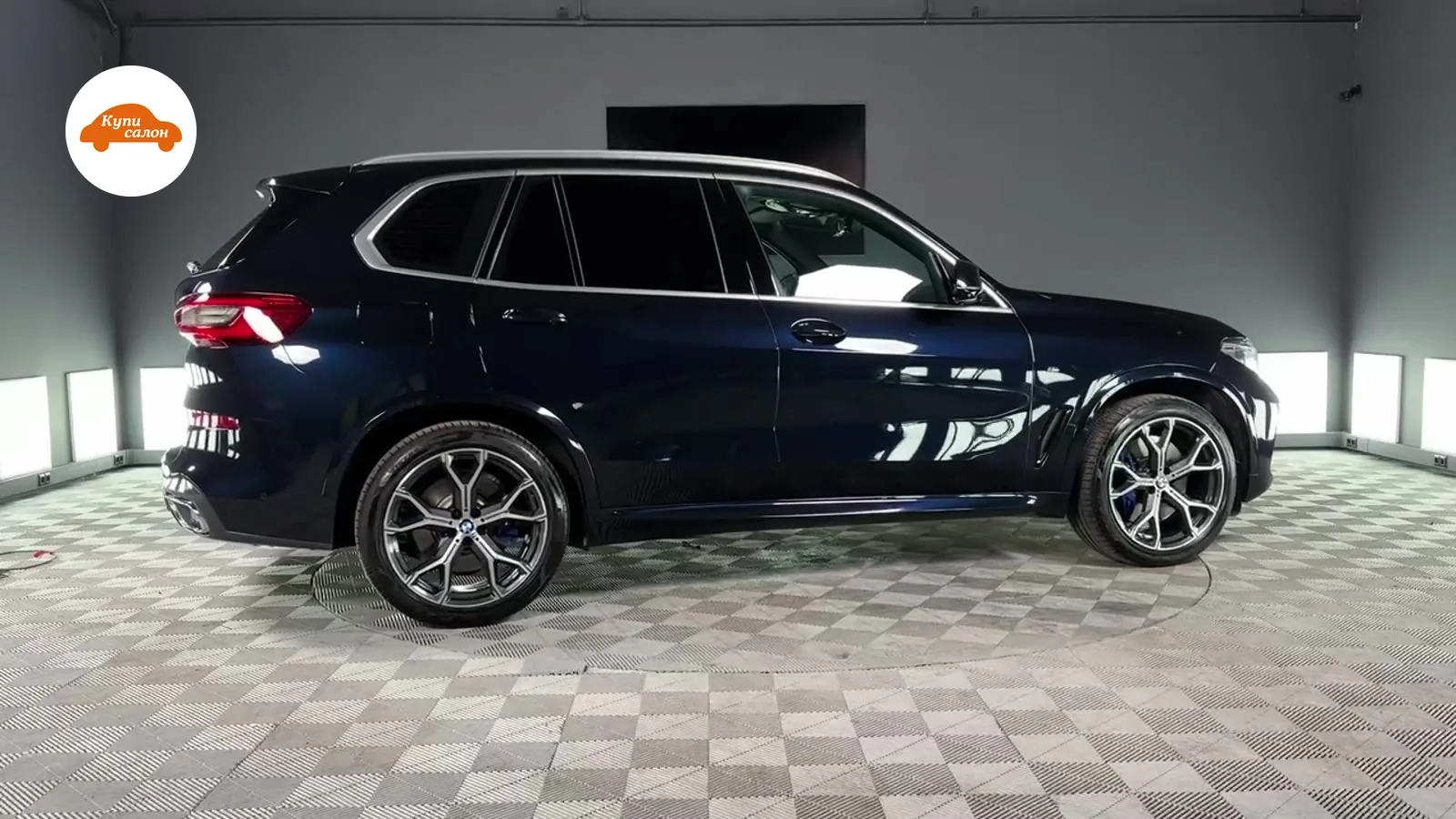 Темно-синий BMW X5, вид сбоку, на поворотной платформе в детейлинг-студии