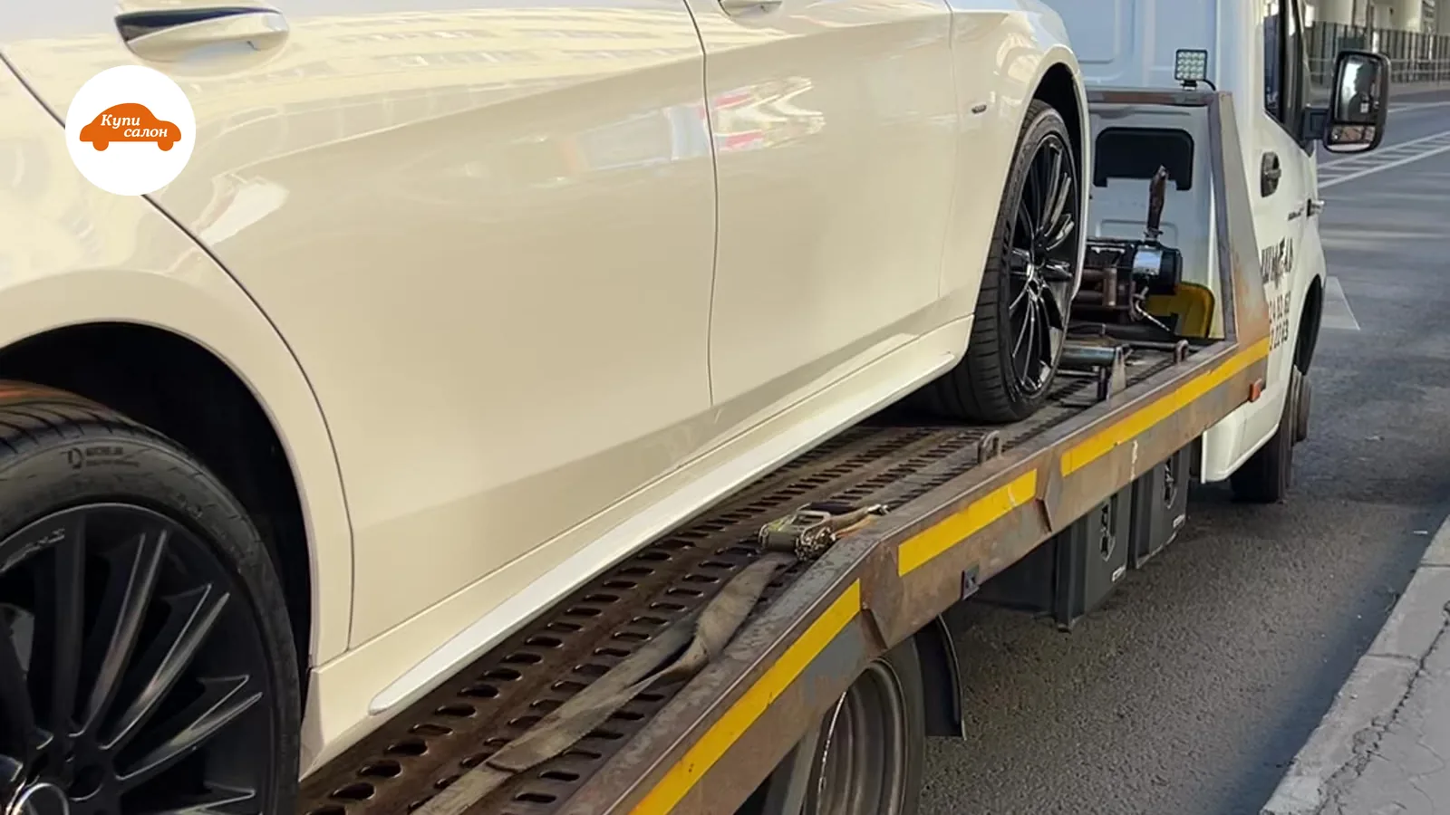 Белый Mercedes-Benz на эвакуаторе, вид сбоку, на фоне эстакады