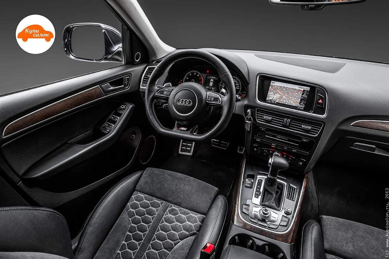 Салон Audi Q5 первого поколения, вид с переднего пассажирского места: руль, передняя панель с экраном, центральная консоль с селектором, сиденье с простёганной серединой