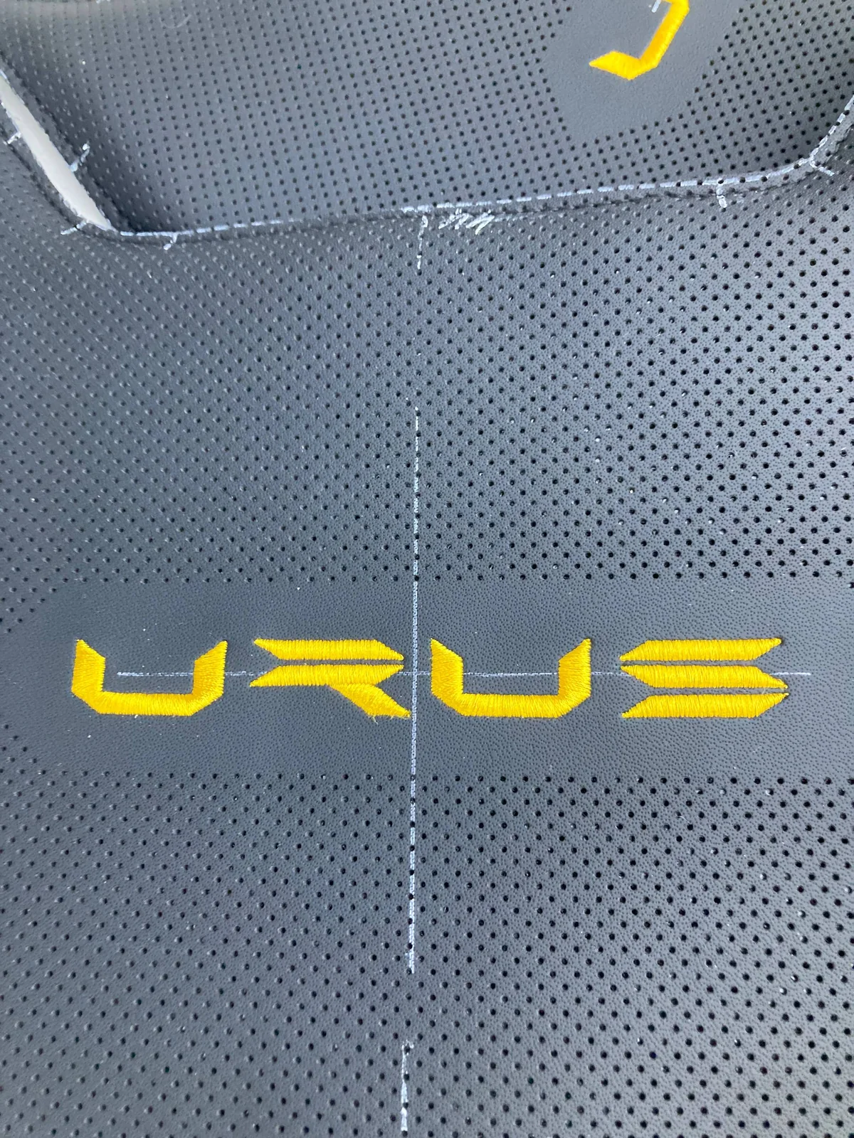 Надпись URUS, вышитая золотой нитью на чёрной перфорированной коже центральной вставки сиденья