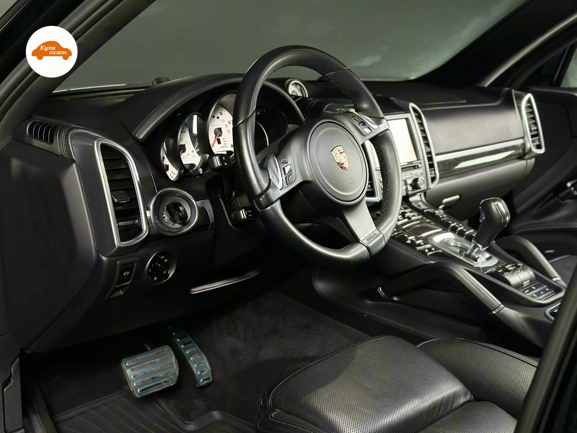 Porsche Cayenne — Интерьер Porsche Cayenne: руль, торпеда, центральная консоль и сиденье водителя в чёрной коже с белой декоративной строчкой