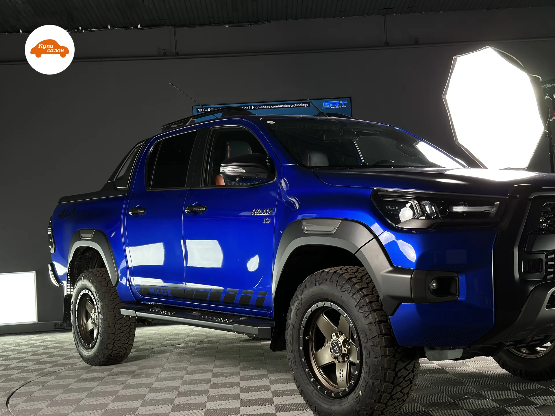 Toyota Hilux — Toyota Hilux синего цвета в цехе автоателье под студийным светом: полная защитная оклейка кузова полиуретановой плёнкой в глянце