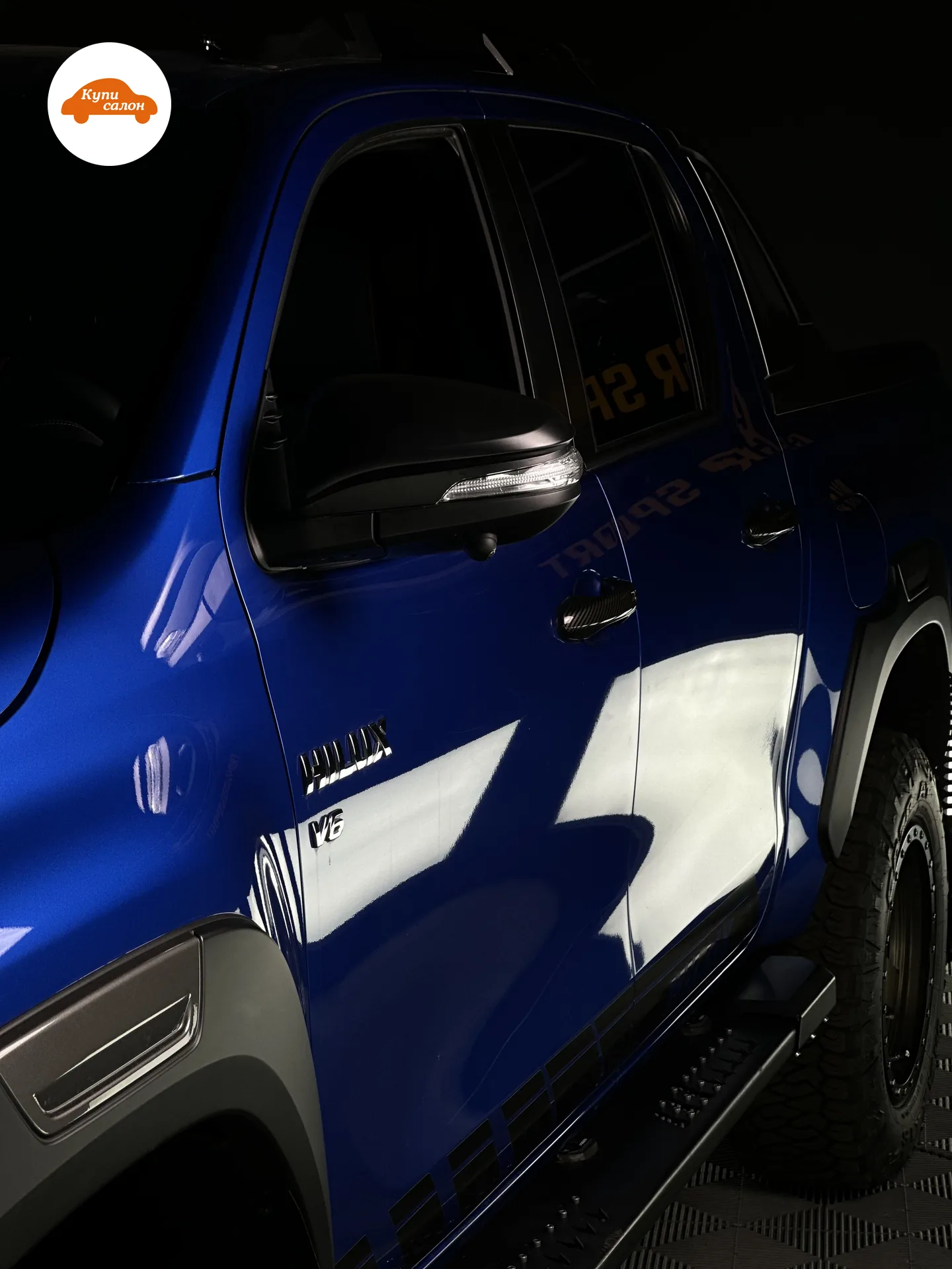 Toyota Hilux — Борт синего Toyota Hilux под защитной плёнкой: двери и пороги оклеены сплошь, чёрный обвес и внедорожные шины владельца