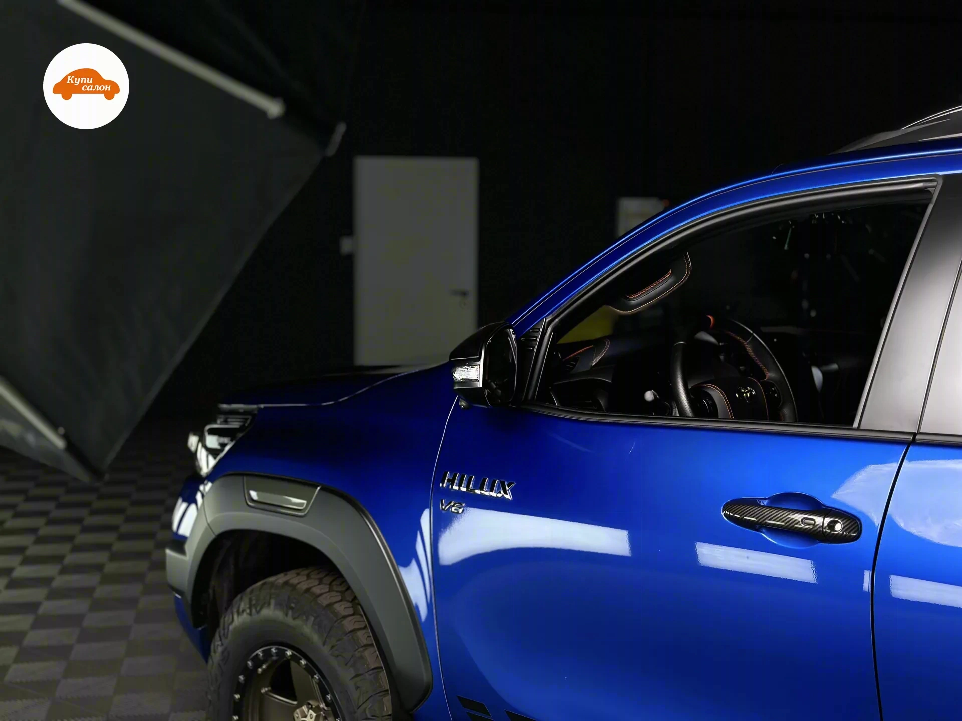 Toyota Hilux — Передняя часть Toyota Hilux и часть салона: карбоновые накладки на ручке двери, перетянутые элементы с оранжевой строчкой — конфигурация владельца