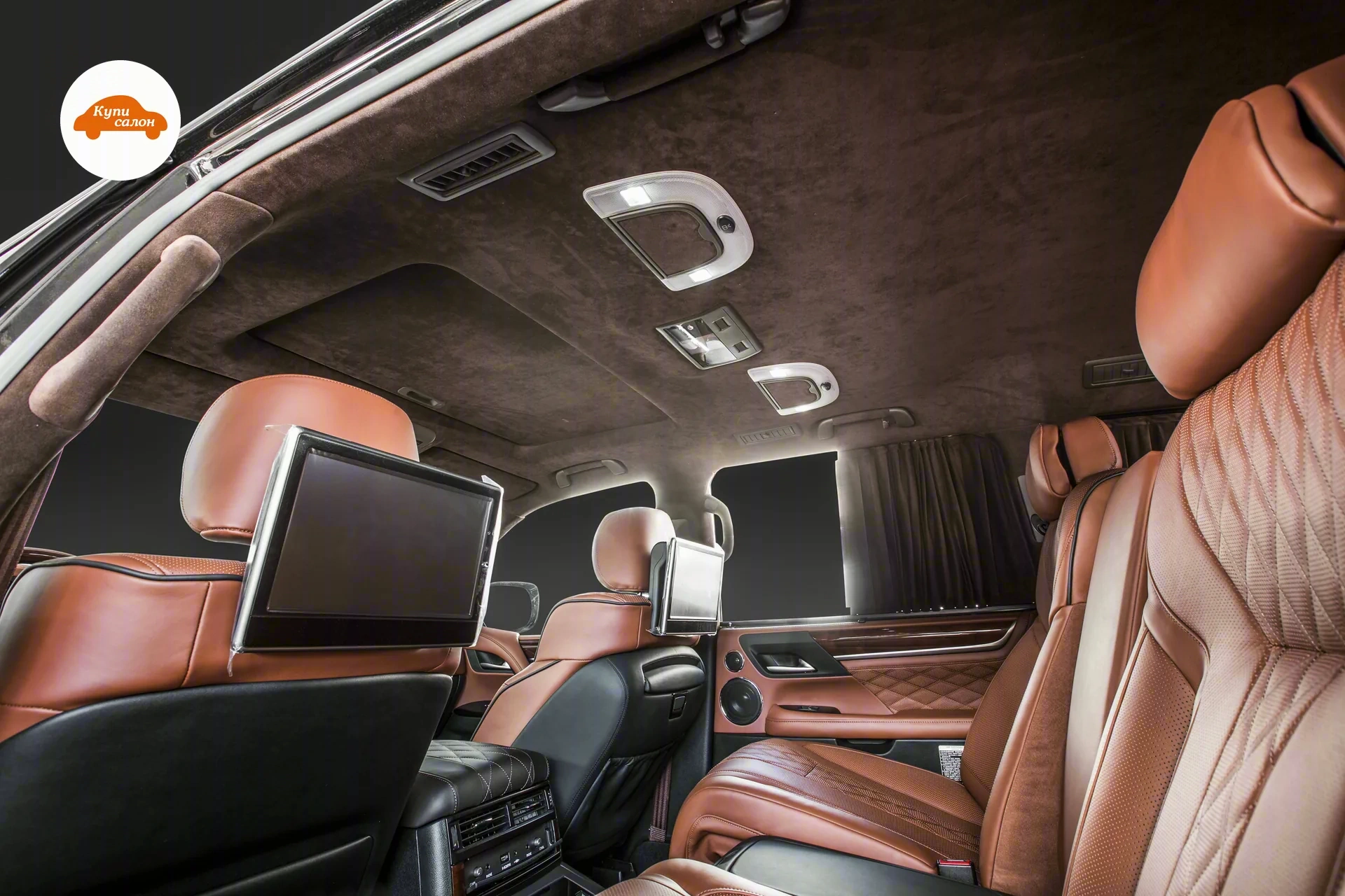 Lexus LX — Задний ряд Lexus LX: сиденья в коричневой и чёрной коже, мониторы в спинках передних кресел, коричневая алькантара на потолке и стойках, центральный подлокотник